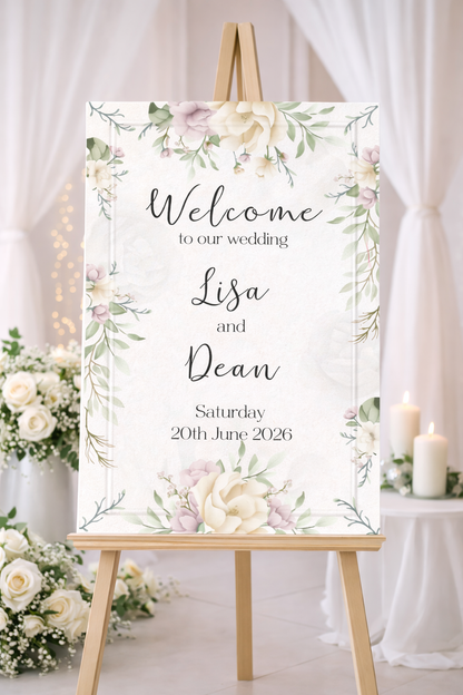 Wedding welcome sign with floral design on an easel, surrounded by flowers and candles.